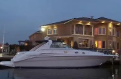 The Image of 1996 Sea Ray 450 Sundancer yacht docked near a luxurious waterfront home at dusk. - 0