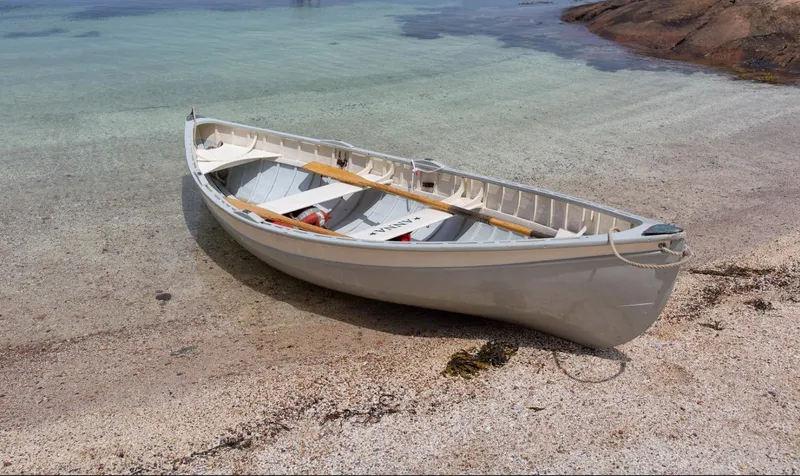 Slide: The Image of A white rowboat on a sandy beach near clear, shallow water. - 26