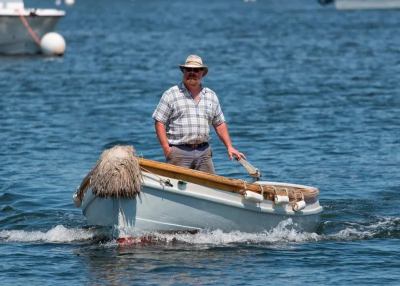 Slide: The Image of Man steering a small boat on water, wearing a hat and plaid shirt. - 27