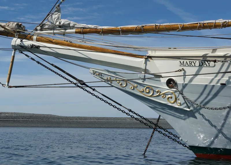 Slide: The Image of Gamage 1962 Coastal Gaff Rigged Schooner, Mary Day, with intricate bow details on calm water. - 4