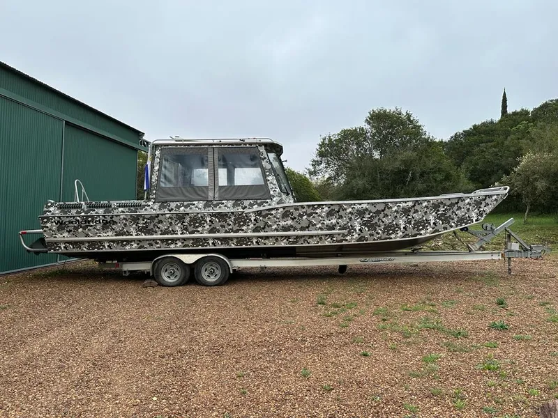 The Image of 2014 Wooldridge 31 boat with camouflage design on a trailer near a green building. - 1