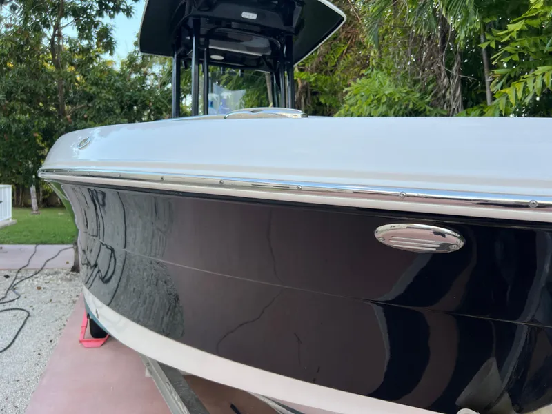 Slide: The Image of 2018 Robalo R242 Center Console boat with sleek black hull, docked outdoors. - 5