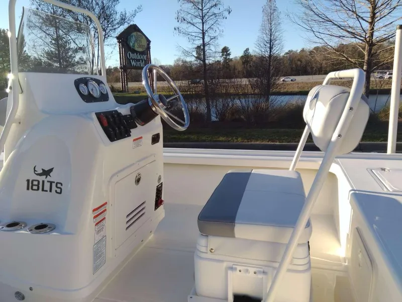 Slide: The Image of 2024 Mako 18 LTS boat interior with steering console and seating, parked near a lake. - 10