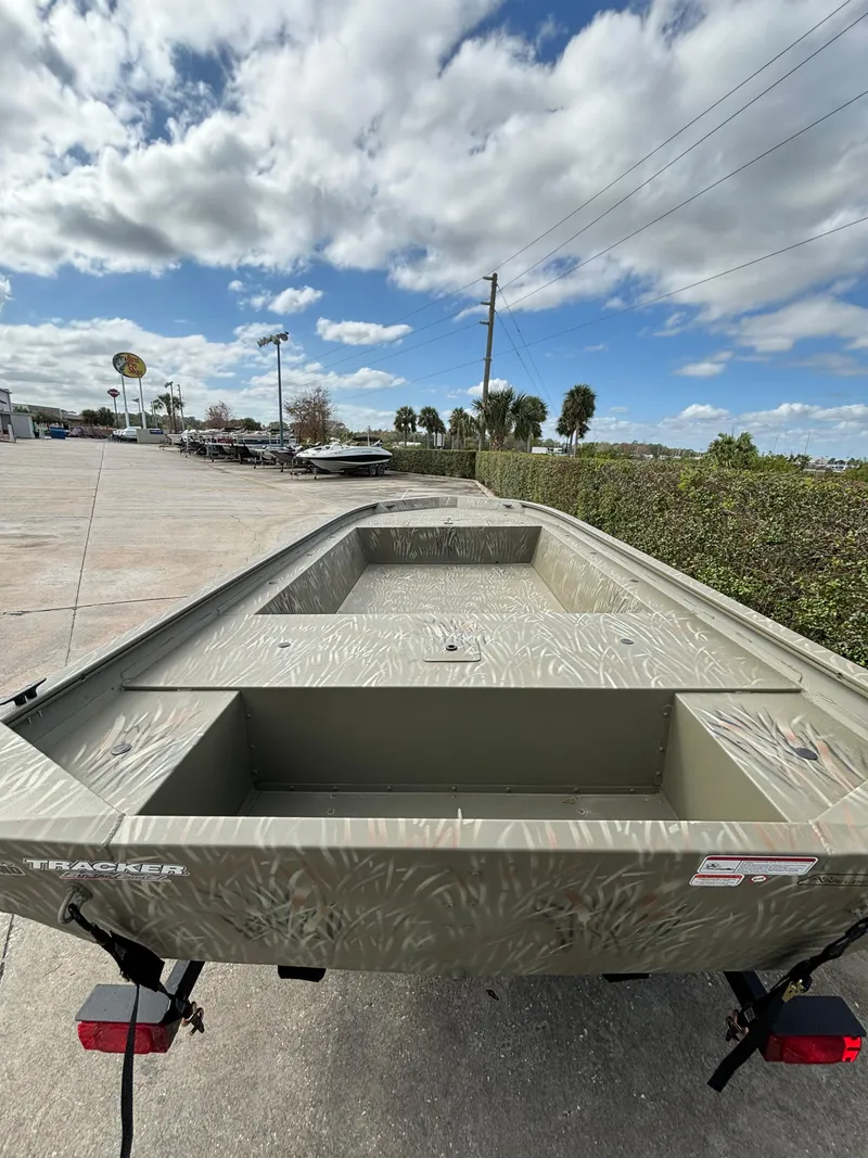 Slide: The Image of 2024 Tracker Grizzly 1754 Jon boat on a trailer, parked outdoors under a cloudy sky. - 2