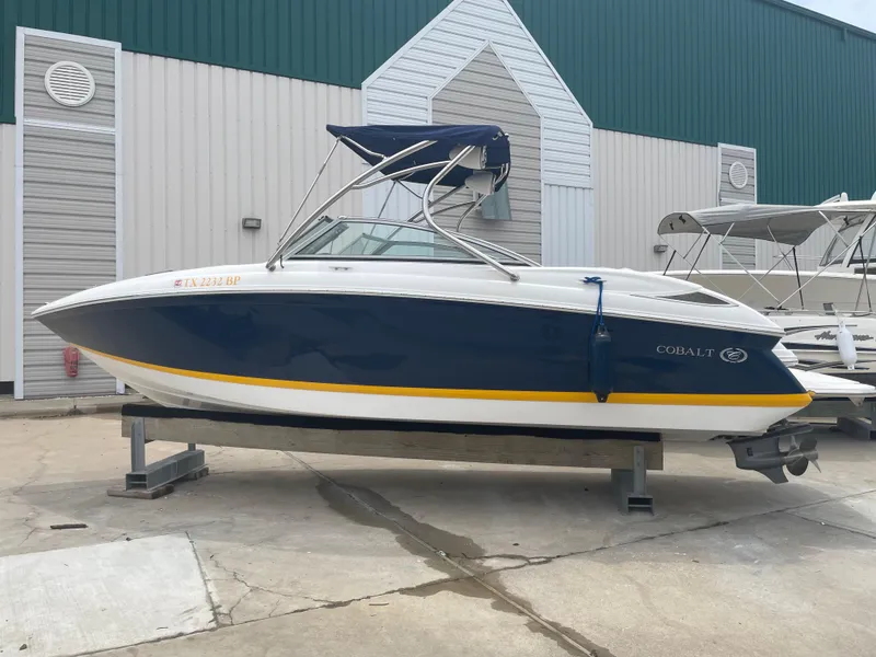 Slide: The Image of 2011 Cobalt 242 boat on a stand, blue and white hull, docked outside. - 46