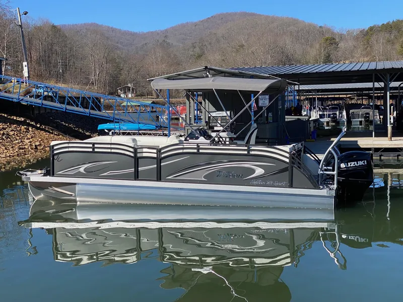 Slide: The Image of 2024 JC Neptoon Sport 23TT pontoon boat docked on a calm lake. - 3
