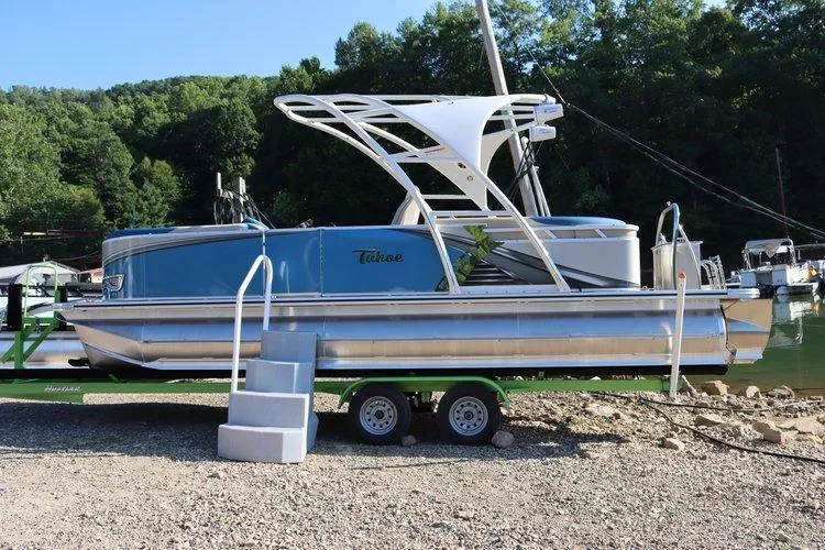 The Image of 2022 Tahoe Pontoon LTZ 2485 QL on trailer by lakeside with lush green background. - 0