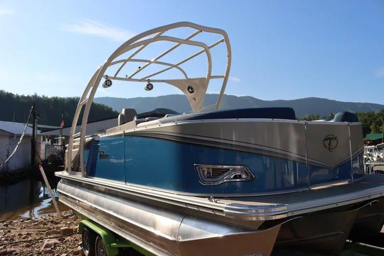 Slide: The Image of 2022 Tahoe Pontoon LTZ 2485 QL boat docked by a lake with mountains in the background. - 2