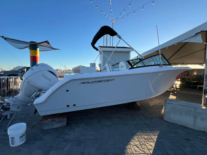 The Image of 2024 Aquasport 2200 DC boat displayed outdoors under clear sky. - 0