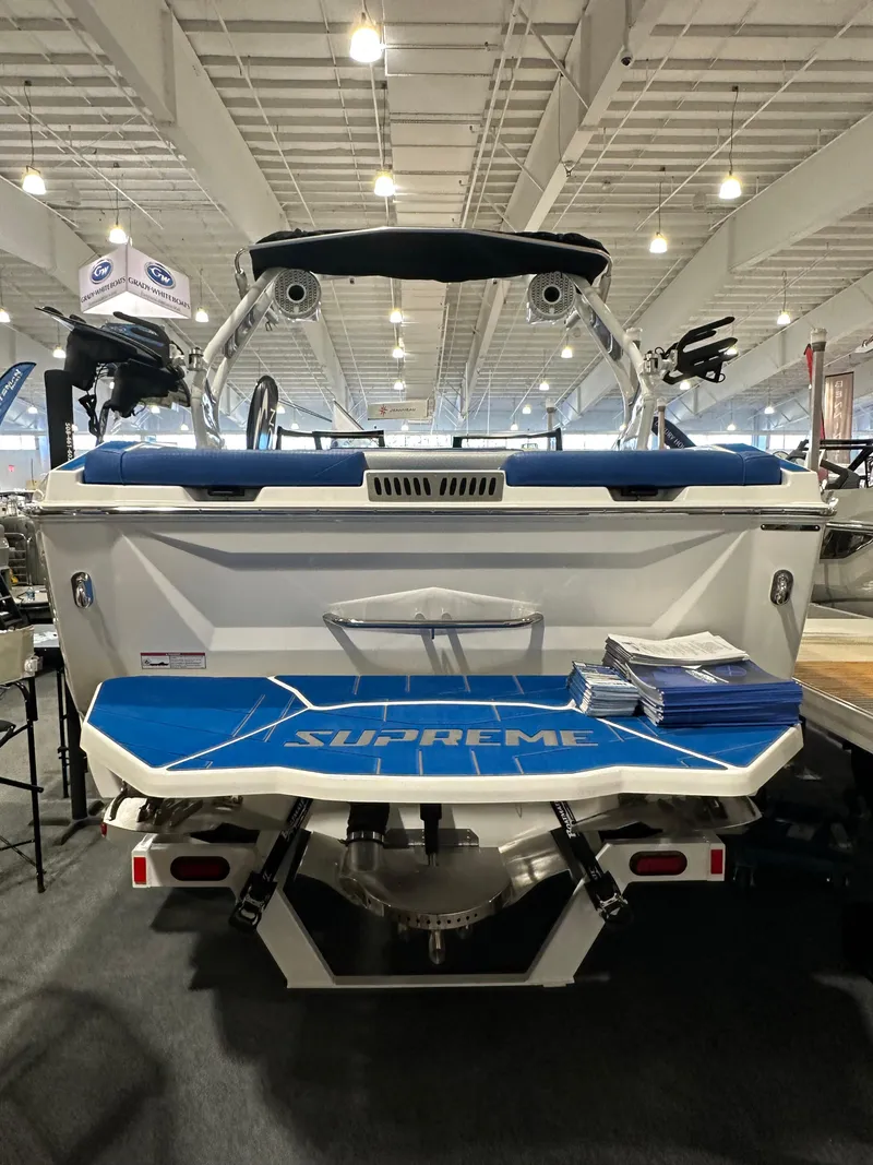 Slide: The Image of 2023 Supreme ZS212 boat displayed indoors, rear view with blue and white design. - 2