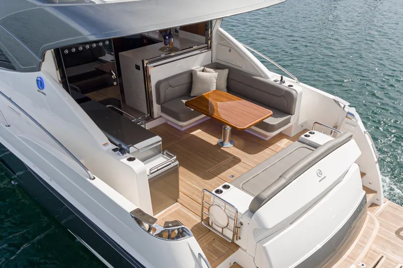 Slide: The Image of 2020 Riviera 5400 Sport Yacht with elegant deck seating and wooden table on calm water. - 19