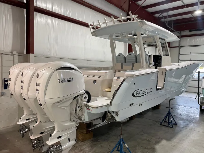 The Image of 2023 Robalo R360 Center Console boat with triple Yamaha engines in a warehouse. - 0