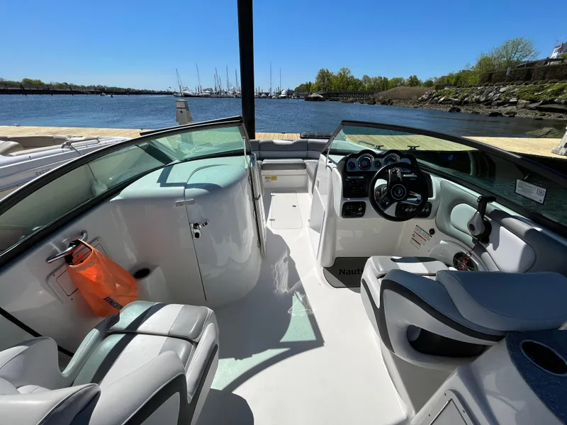 Slide: The Image of 2021 NauticStar 243DC Sport Deck boat interior with steering wheel and seating, docked by the water. - 9