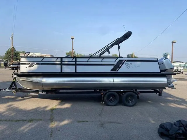 Slide: The Image of 2023 Viaggio LAGO 22F pontoon boat on a trailer in a parking lot. - 2