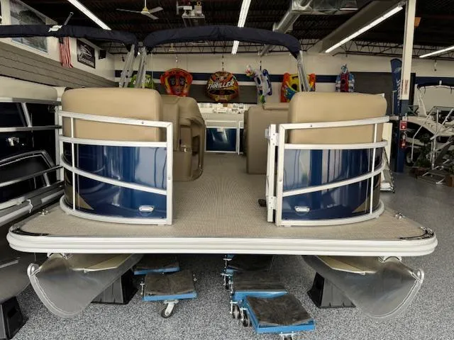 Slide: The Image of 2024 Starcraft LX 20 R pontoon boat in showroom, featuring beige seating and blue accents. - 2