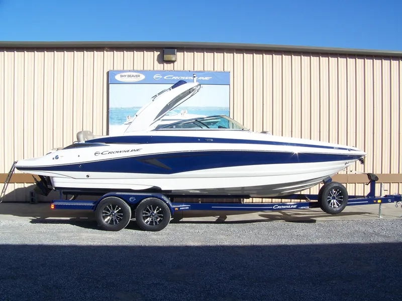 The Image of 2024 Crownline 280 boat on trailer, parked outside a beige building. - 1