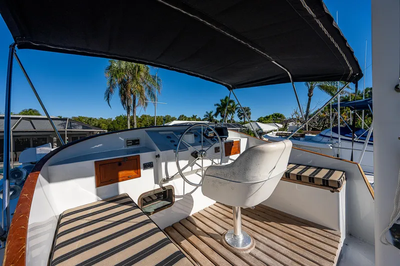 Slide: The Image of 1983 Krogen 42 yacht helm with striped seating and canopy, surrounded by palm trees. - 16