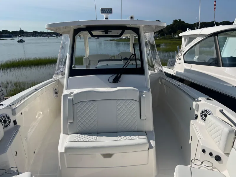 Slide: The Image of 2024 Pursuit S 328 Sport boat with white seating, docked by a serene waterfront. - 10