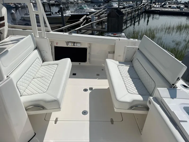 Slide: The Image of 2024 Pursuit S 328 Sport boat interior with white cushioned seating and marina background. - 25