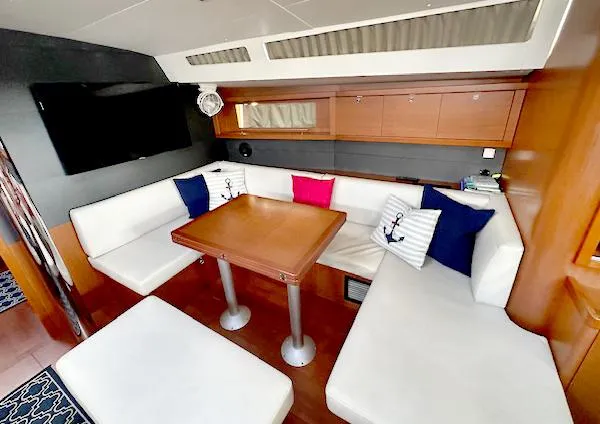 Slide: The Image of 2019 Beneteau Oceanis 48 interior with white seating, wooden table, and nautical-themed cushions. - 21