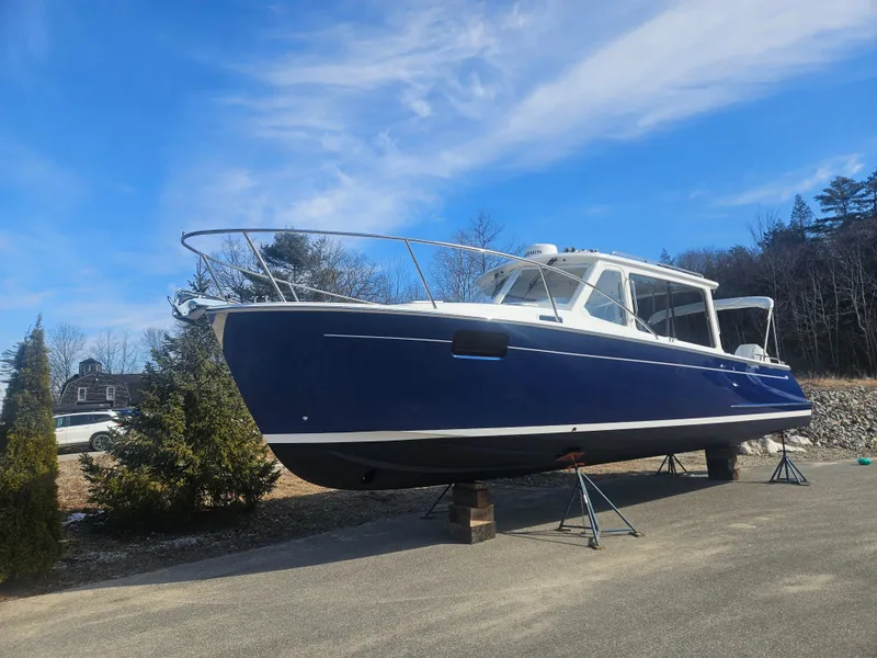 Slide: The Image of 2024 MJM 35 boat on stands, blue hull, white cabin, clear sky background. - 22