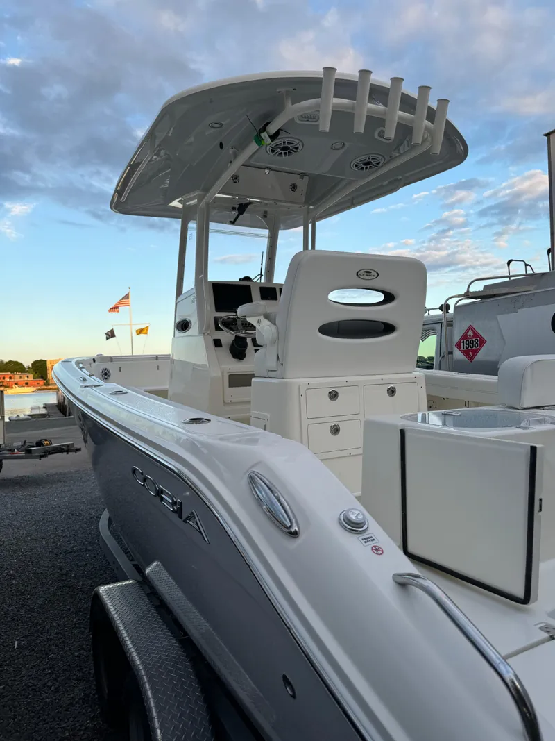 Slide: The Image of 2024 Cobia 240 Center Console boat with T-top and rod holders, docked under a blue sky. - 20