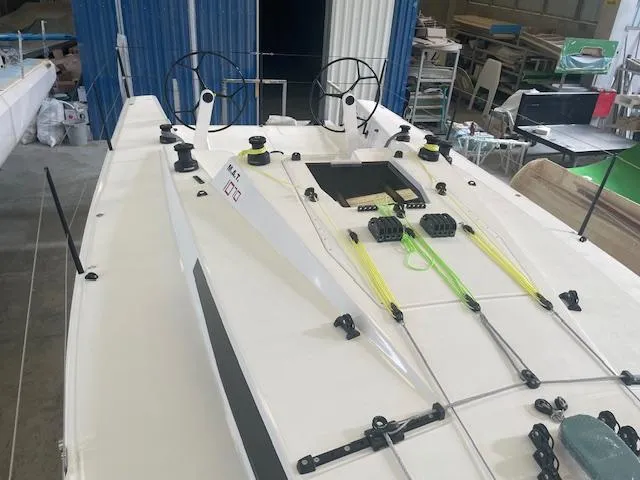 Slide: The Image of 2024 M.A.T. 1070 sailboat deck with dual steering wheels in a workshop. - 12