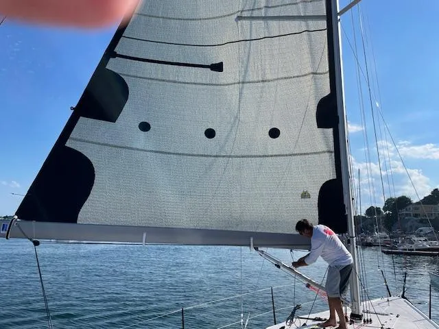 Slide: The Image of Man adjusting sail on M.A.T. 1070 sailboat, 2024 model, in sunny marina. - 17