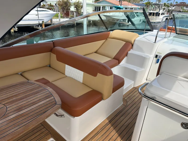 Slide: The Image of 2014 Sea Ray 370 Venture boat interior with tan and brown seating, wooden table, and dock view. - 36