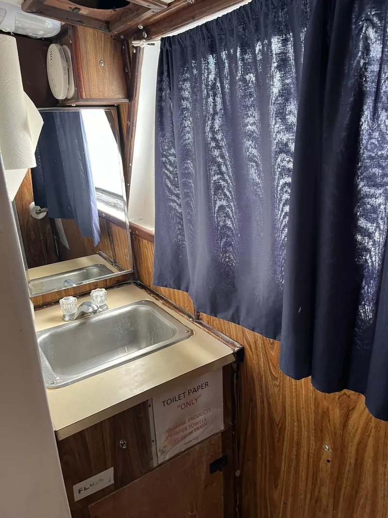 Slide: The Image of 1983 Swiftships Charter Boat bathroom with sink, mirror, and blue curtains. - 18