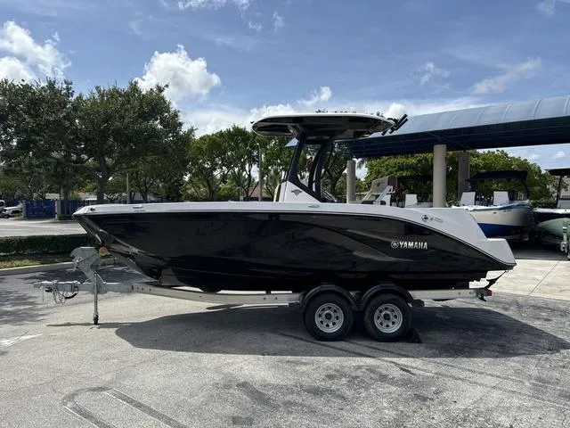 Slide: The Image of 2024 Yamaha Boats 222 FSH Sport E on trailer, black hull, displayed at dealership. - 2