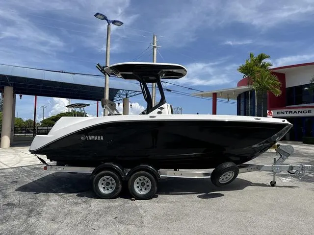 Slide: The Image of 2024 Yamaha Boats 222 FSH Sport E, rear view, white exterior, docked under canopy. - 6