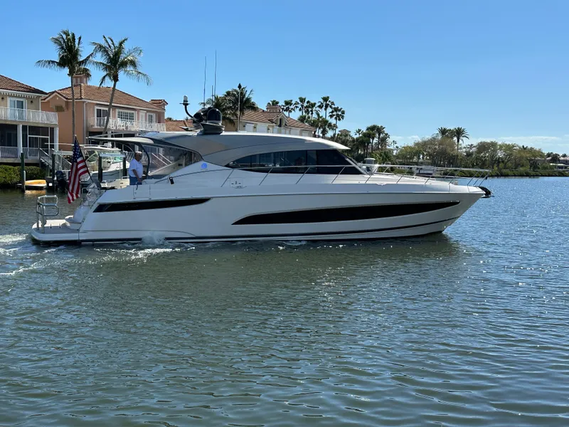 Slide: The Image of 2022 Riviera Sport Yacht 5400 Platinum Edition cruising on a sunny day near waterfront homes. - 1