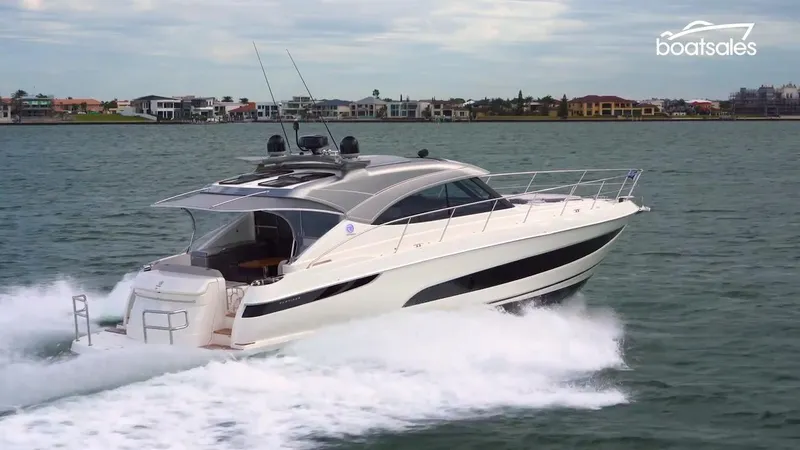 Slide: The Image of 2022 Riviera Sport Yacht 5400 Platinum Edition cruising on water near coastal homes. - 12