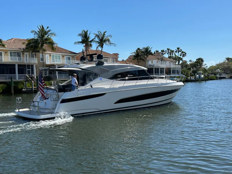 Slide: The Image of 2022 Riviera Sport Yacht 5400 Platinum Edition cruising near waterfront homes. - 2