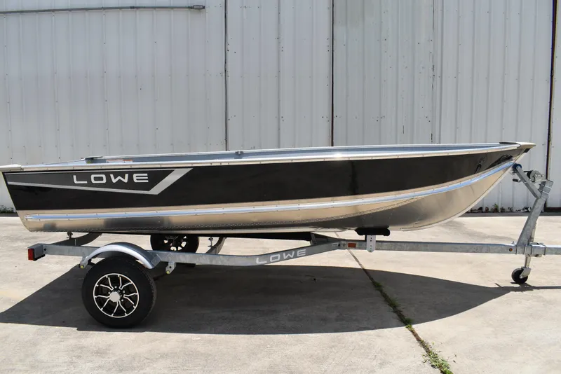 The Image of 2024 Lowe WV 1470 boat on trailer, black and silver design, parked outdoors. - 0