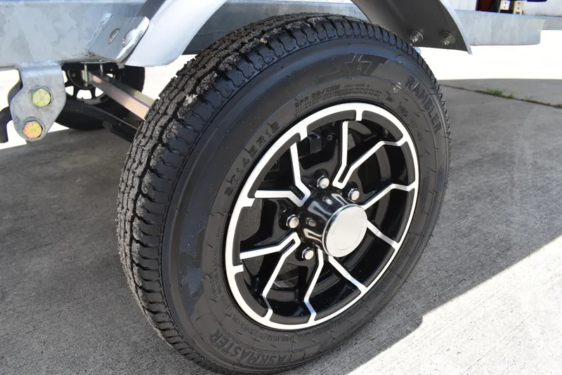 Slide: The Image of 2024 Lowe WV 1470 trailer wheel with black and silver rim on concrete surface. - 15