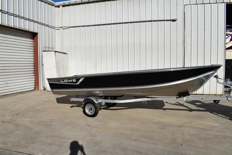The Image of 2024 Lowe WV 1670 boat on trailer outside metal building. - 1