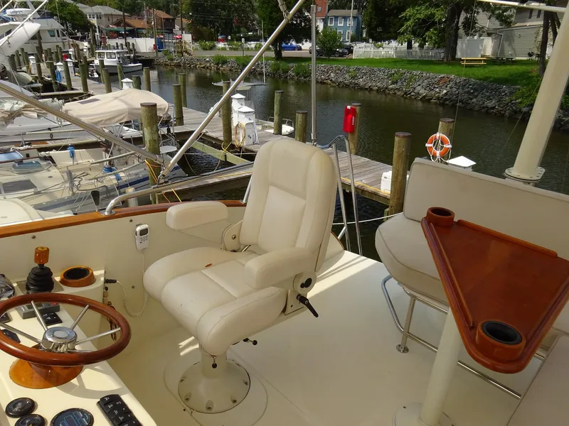 Slide: The Image of Captain's chair and helm on 2002 Hinckley Talaria 44 FB yacht, docked by a serene marina. - 11