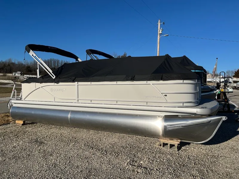 Slide: The Image of 2024 Sweetwater 2286SB pontoon boat with black canopy, parked on gravel. - 0