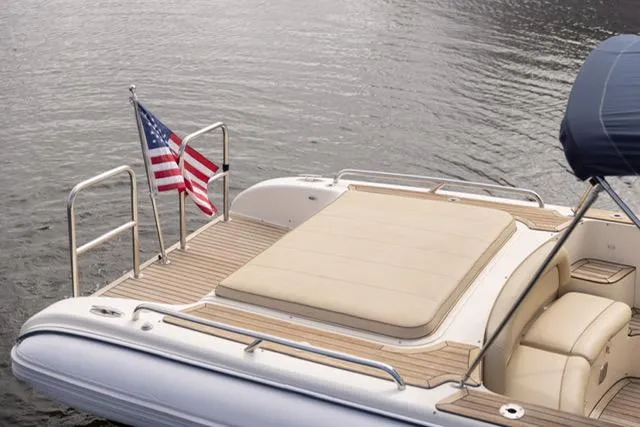 Slide: The Image of 2007 Novurania Chase boat with American flag, featuring a sun deck and cushioned seating. - 5