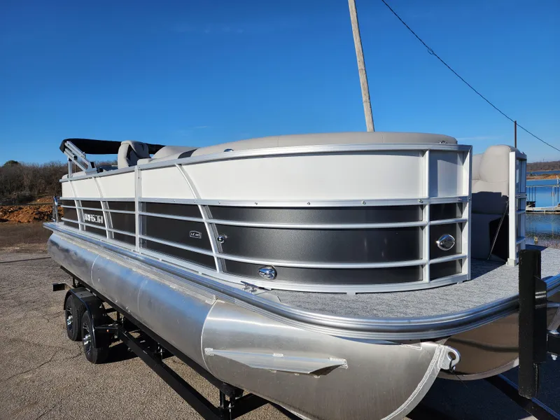 The Image of 2024 Trifecta 24RF LE 2 75 pontoon boat on trailer, docked by a lake. - 0