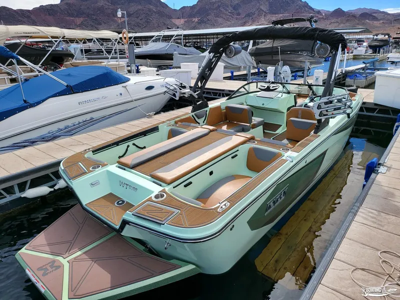 Slide: The Image of 2022 Heyday WT-Surf boat docked at marina, surrounded by other boats and scenic mountains. - 8