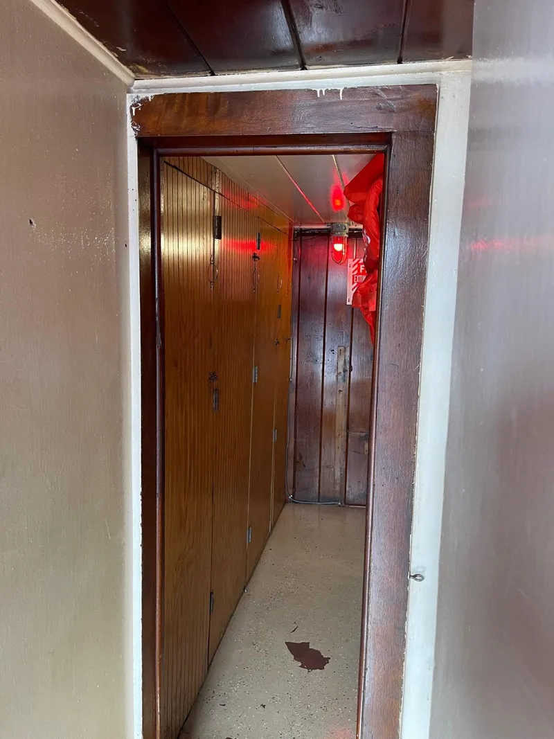 Slide: The Image of Narrow hallway inside a 1961 Commercial Model Bow Tug with wooden paneling and red lighting. - 14