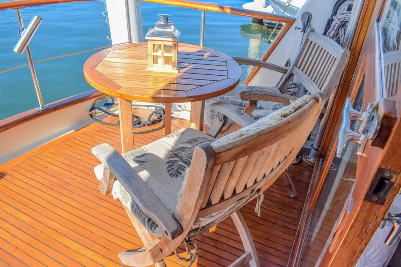 Slide: The Image of 1984 Angel Defever LRC yacht deck with wooden chairs and table, overlooking calm water. - 13