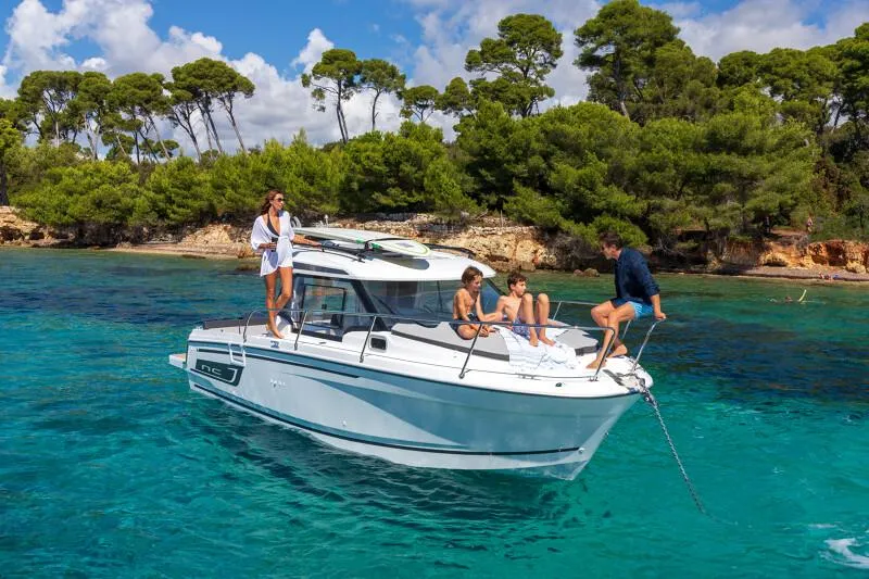 Slide: The Image of 2024 Jeanneau NC 795 Weekender S2 boat cruising in clear blue waters near a forested shoreline. - 3