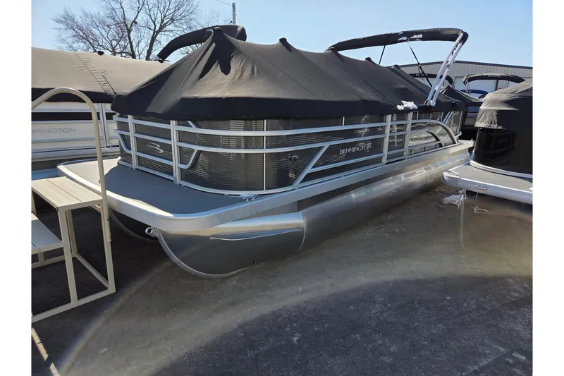 Slide: The Image of 2024 Bennington 22SVSR pontoon boat with black cover, parked outdoors. - 0