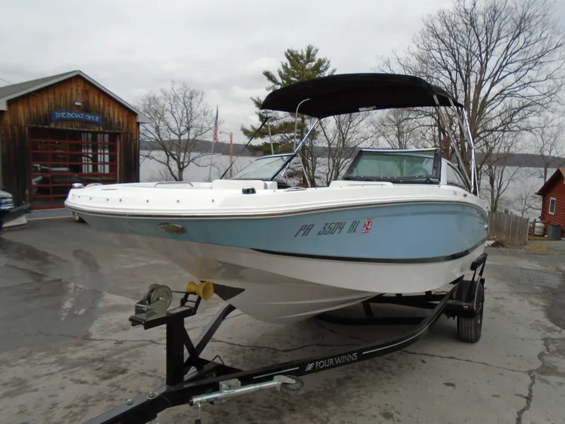 Slide: The Image of 2022 Four Winns HD2 boat on trailer near lake and wooden building. - 1
