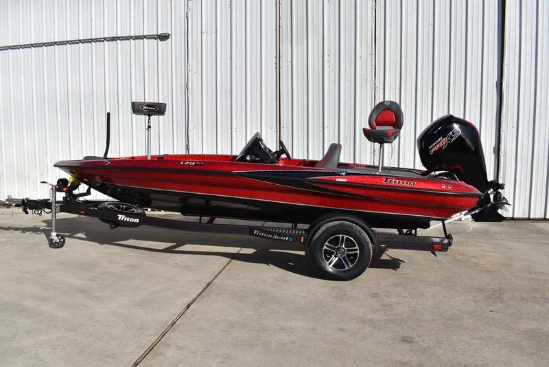 Slide: The Image of 2024 Triton 179 TrX bass boat in red on a trailer, parked outdoors. - 2