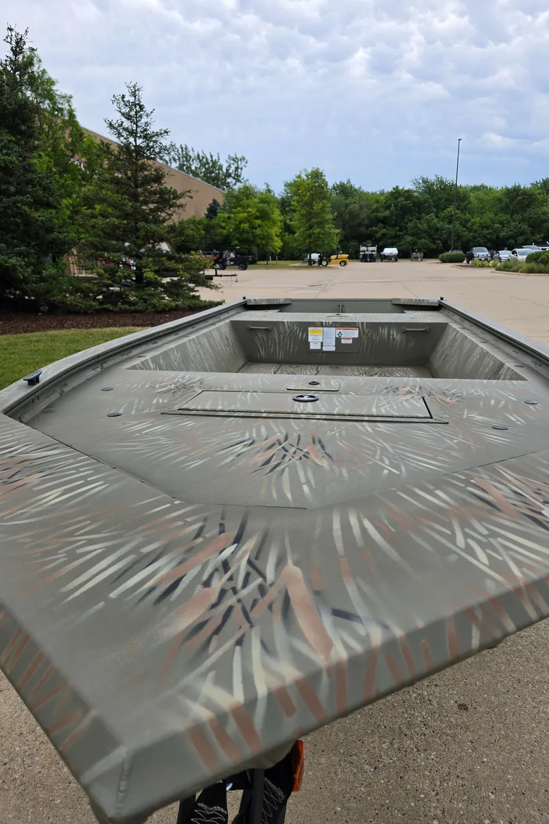 Slide: The Image of 2024 Tracker Grizzly 1648 Jon boat in a parking lot with a camo pattern. - 2